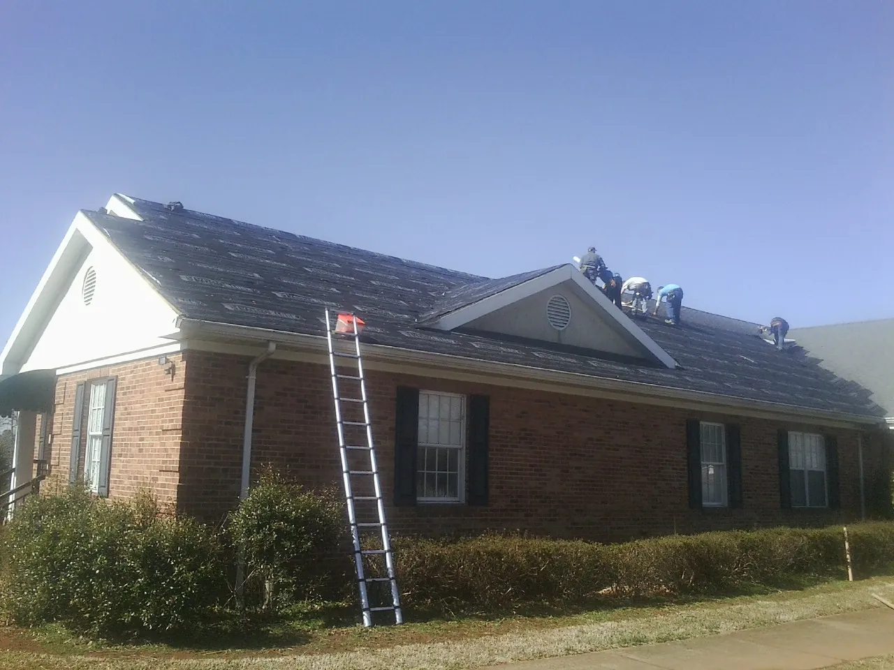 Crew tearing shingles off a brick ranch roof with a ladder set — Metal Roof Repair work by our crew in Mc Veytown