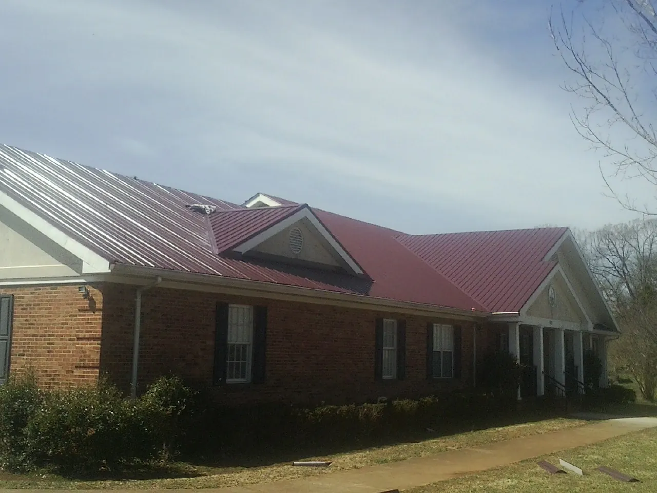 Red metal roof with gabled entries on a long brick building, from a Hail Damage Roof Repair job in Mc Veytown