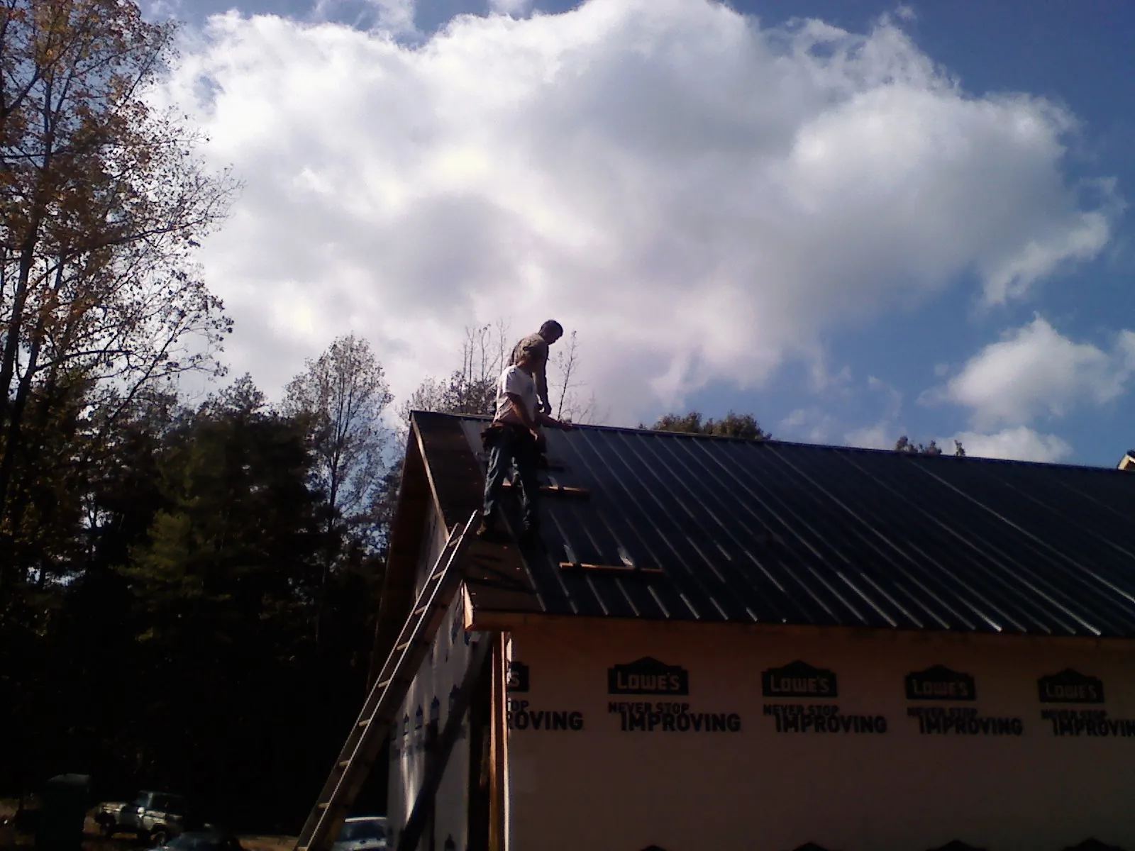 Roofer fastening dark metal panels high against a cloudy sky, from a Roof Inspection job in Mc Veytown