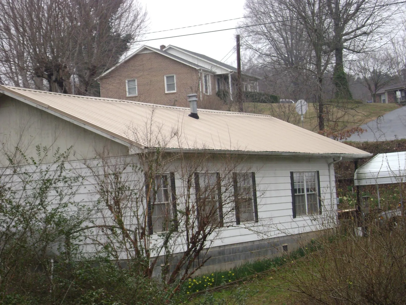 Tan metal roof on a white sided house set into a hillside — Commercial Roofing by Roofing Brothers in Mc Veytown